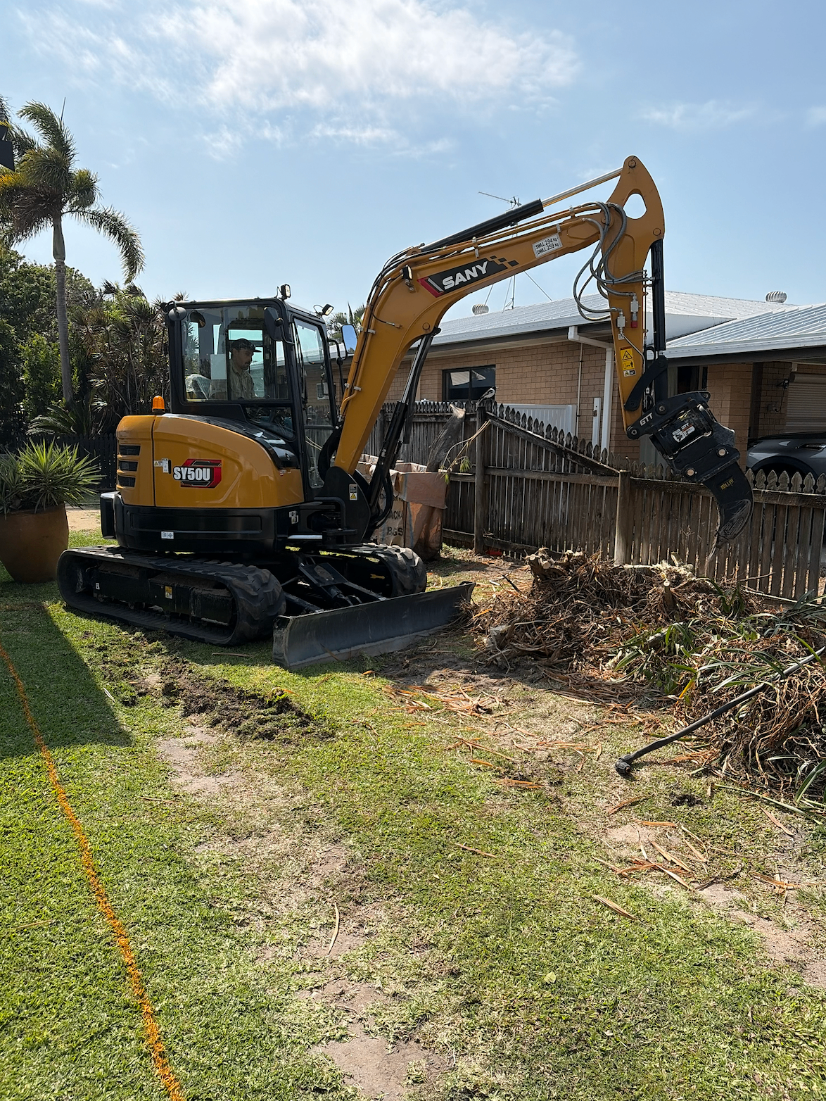 Excavator clearing stumps and green waste from a Mackay backyard