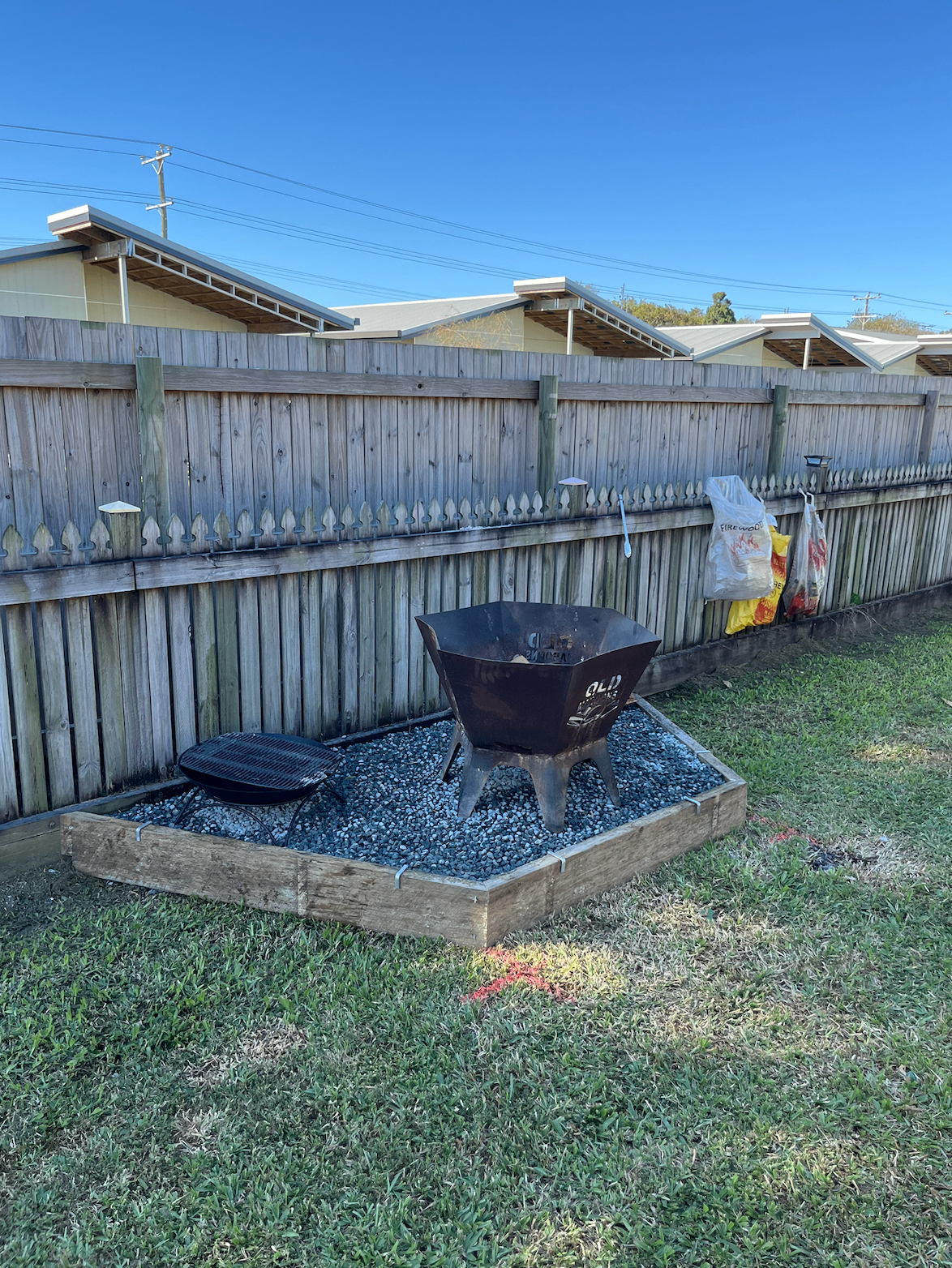 Timber-edged gravel fire pit area built into a Mackay backyard lawn