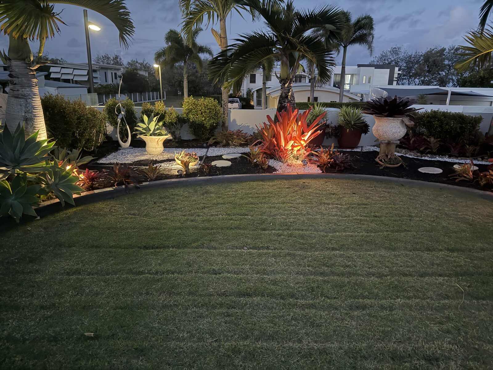 Manicured lawn framed by lit landscaped garden beds